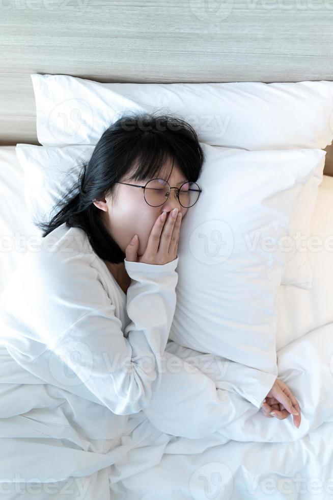 mulher asiática de óculos está bocejando depois de acordar na cama pela manhã. foto