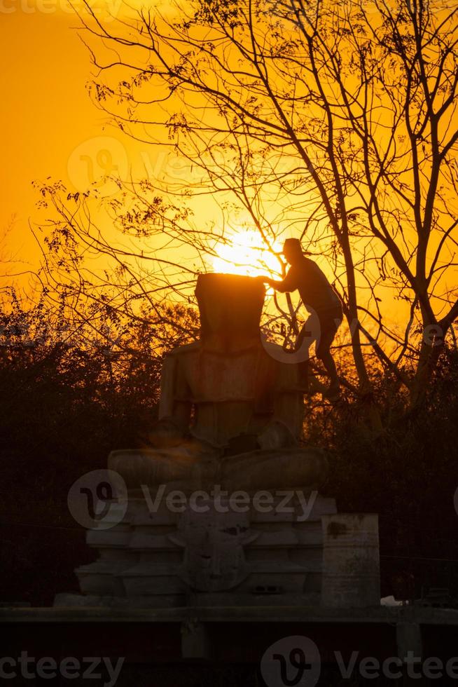 estátua de buda de silhueta e trabalhador asiático, ele está trabalhando e lançando estátua de buda no fundo do pôr do sol crepuscular. tailândia. foto