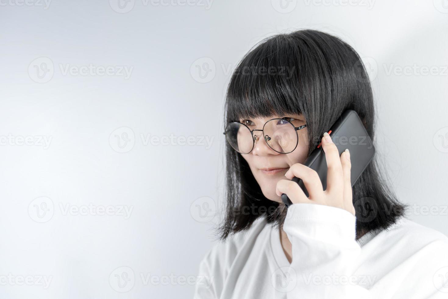 mulher de óculos muito asiática isolada fala e fala na linha com seu celular em fundo branco na luz do estúdio. foto