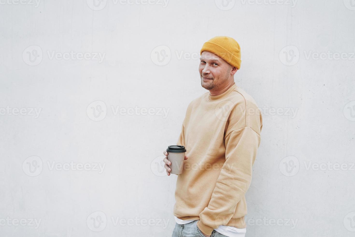 retrato de homem elegante hipster de chapéu amarelo com papel xícara de café na cidade foto