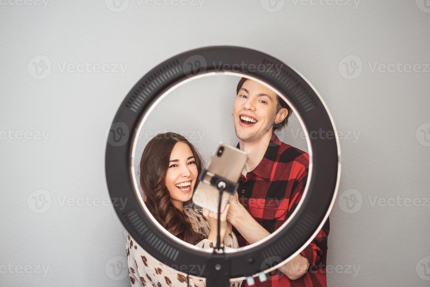 jovem casal de blogueiros de beleza, cabeleireiro, cabeleireiro e modelo com fotos de estilo de cabelo no celular com lâmpada de anel no fundo da parede cinza
