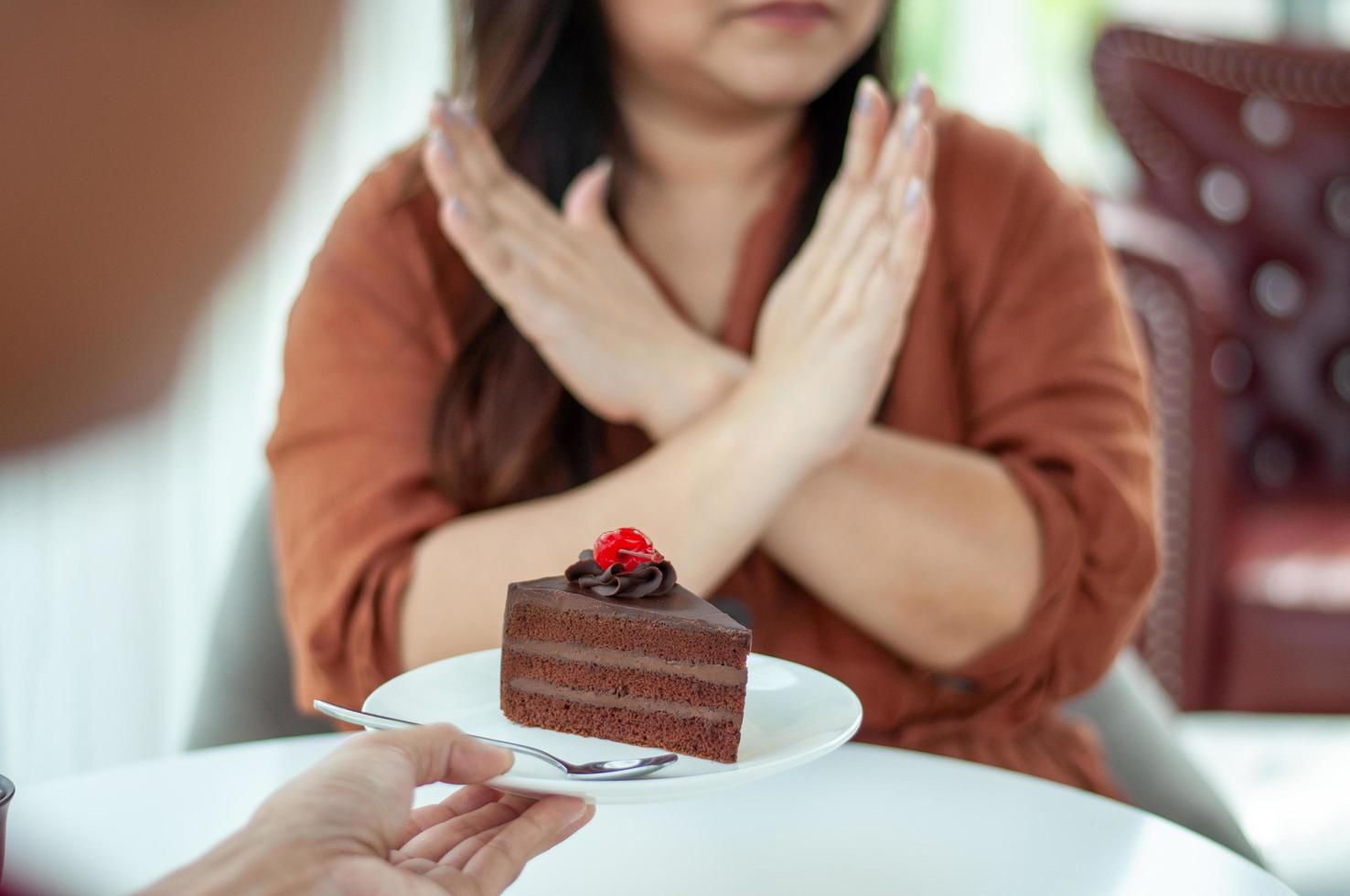 mulher gorda empurra o prato sobre um bolo de chocolate. intenção de perder peso para uma boa saúde e boa forma foto