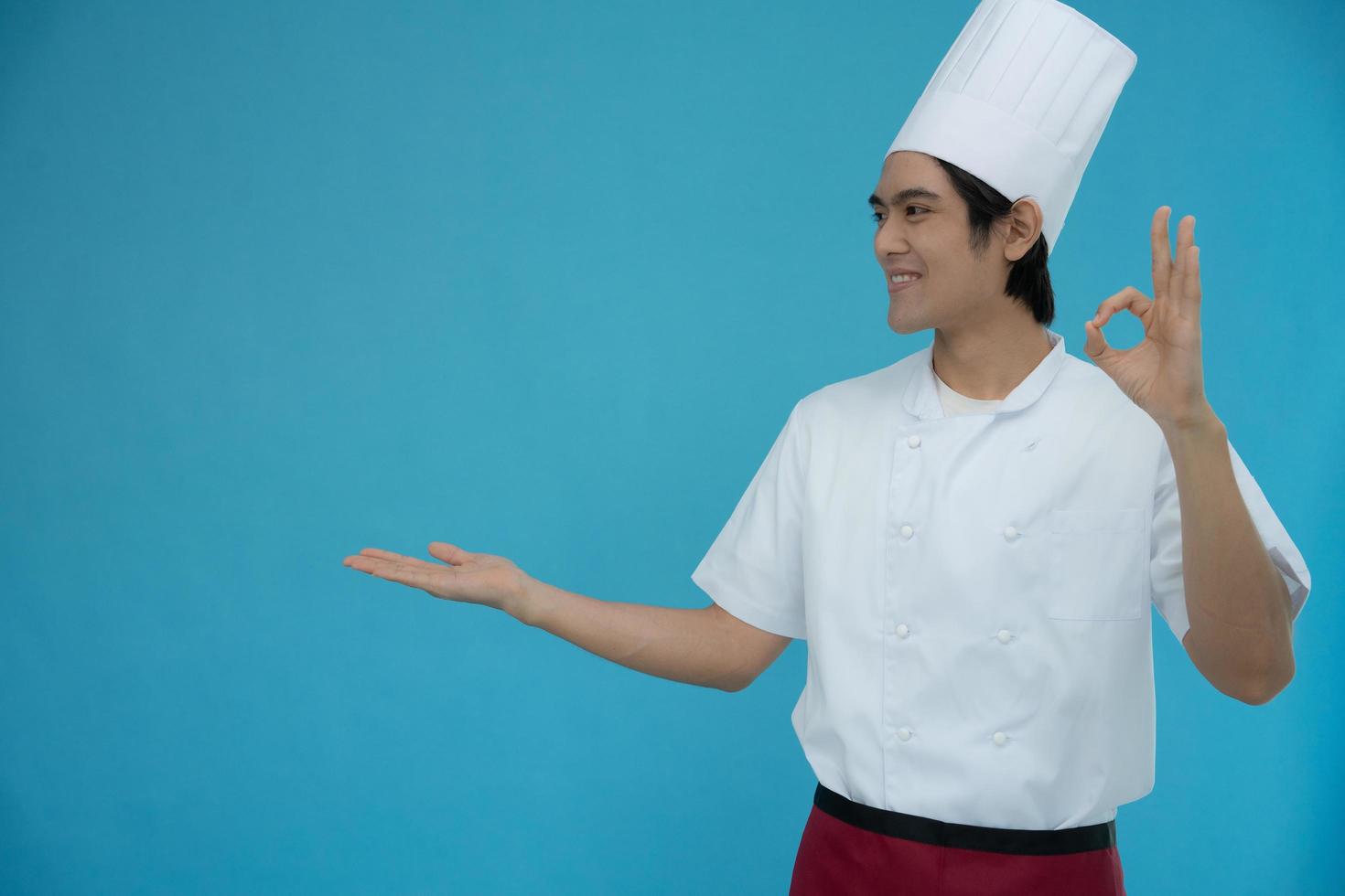 retrato de um homem asiático bonito vestindo roupas de chef em fundo azul isolado. chef sorri e fica feliz com a comida que está bem com a apresentação. foto