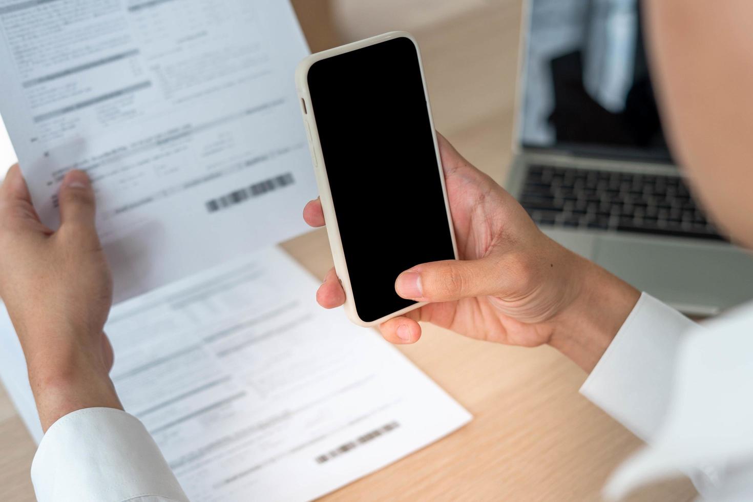 um homem de negócios usa seu telefone para digitalizar um código de barras para pagar sua fatura mensal de cartão de crédito após receber uma fatura. conceito de pagamento de contas on-line foto