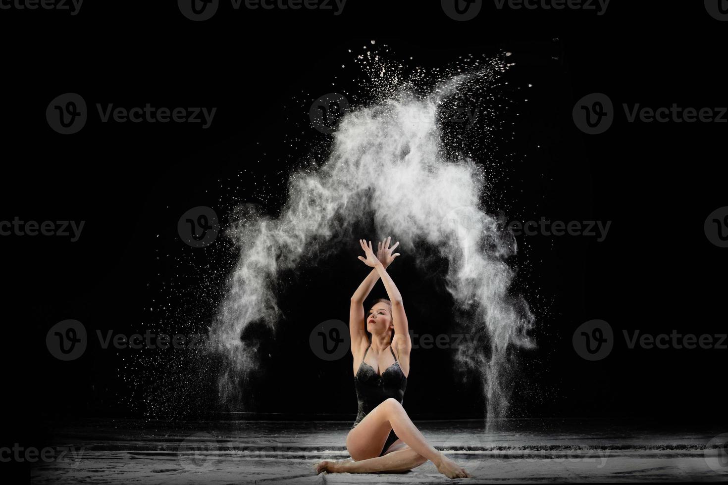 jovem mulher bonita com farinha espalhada no ar em um fundo preto foto
