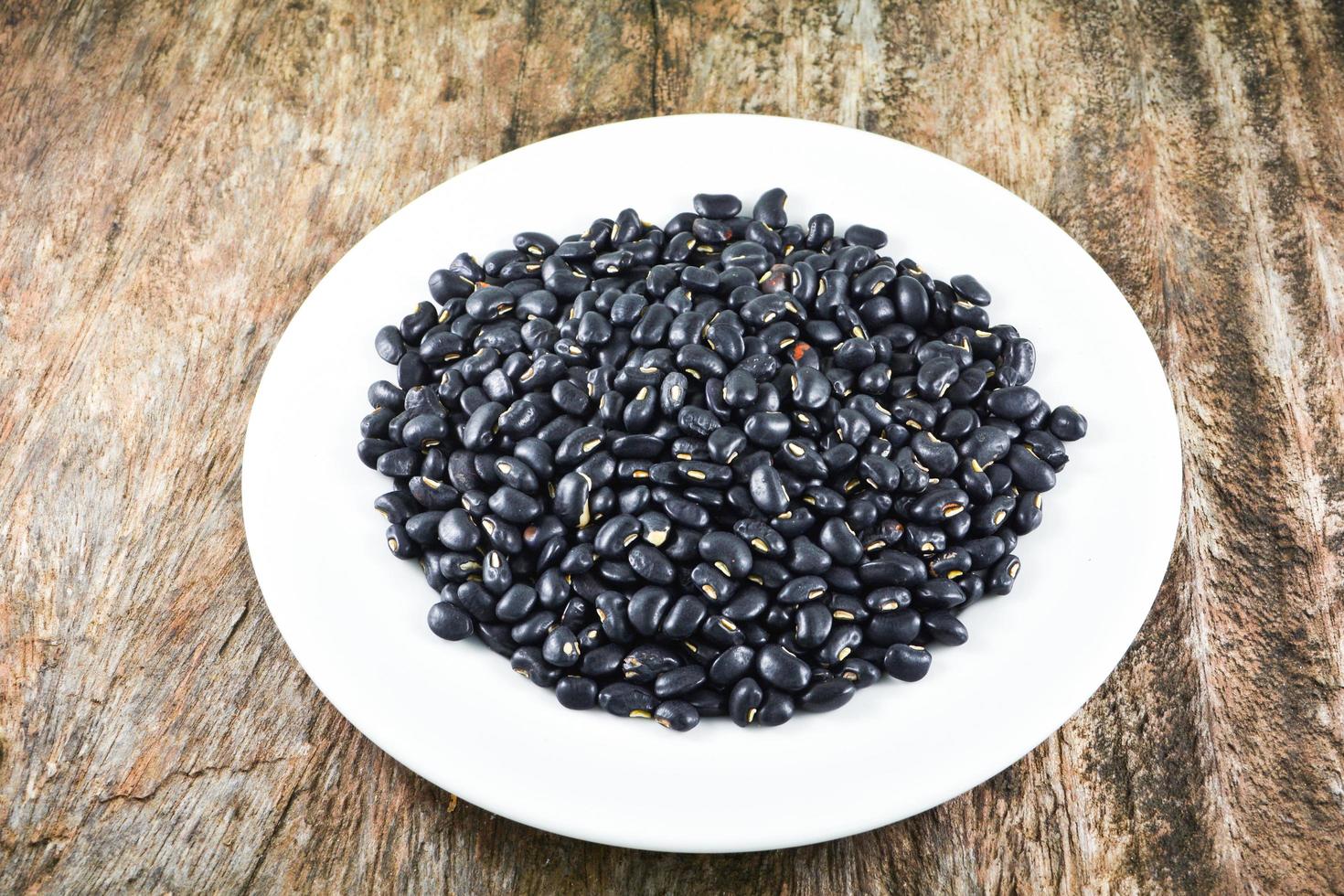 sementes de grãos de feijão preto na comida de prato branco sobre fundo de madeira foto