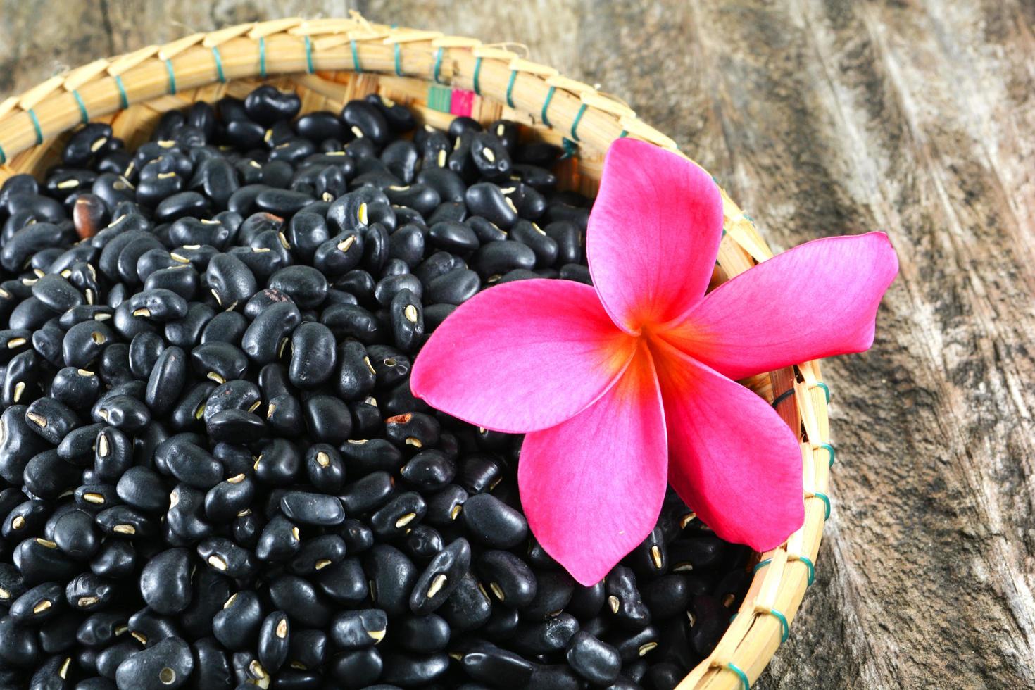 sementes de grãos de feijão preto na cesta com flor rosa em fundo de madeira foto