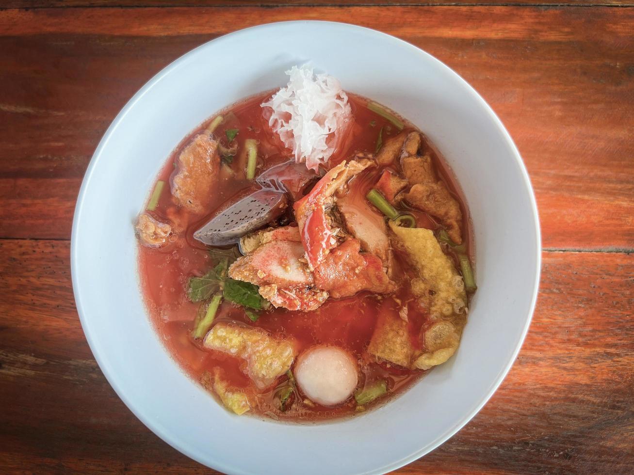 macarrão de estilo tailandês de comida com tofu variado e bola de peixe em sopa vermelha - macarrão plano de frutos do mar rosa estilo de comida asiática na tigela de sopa foto