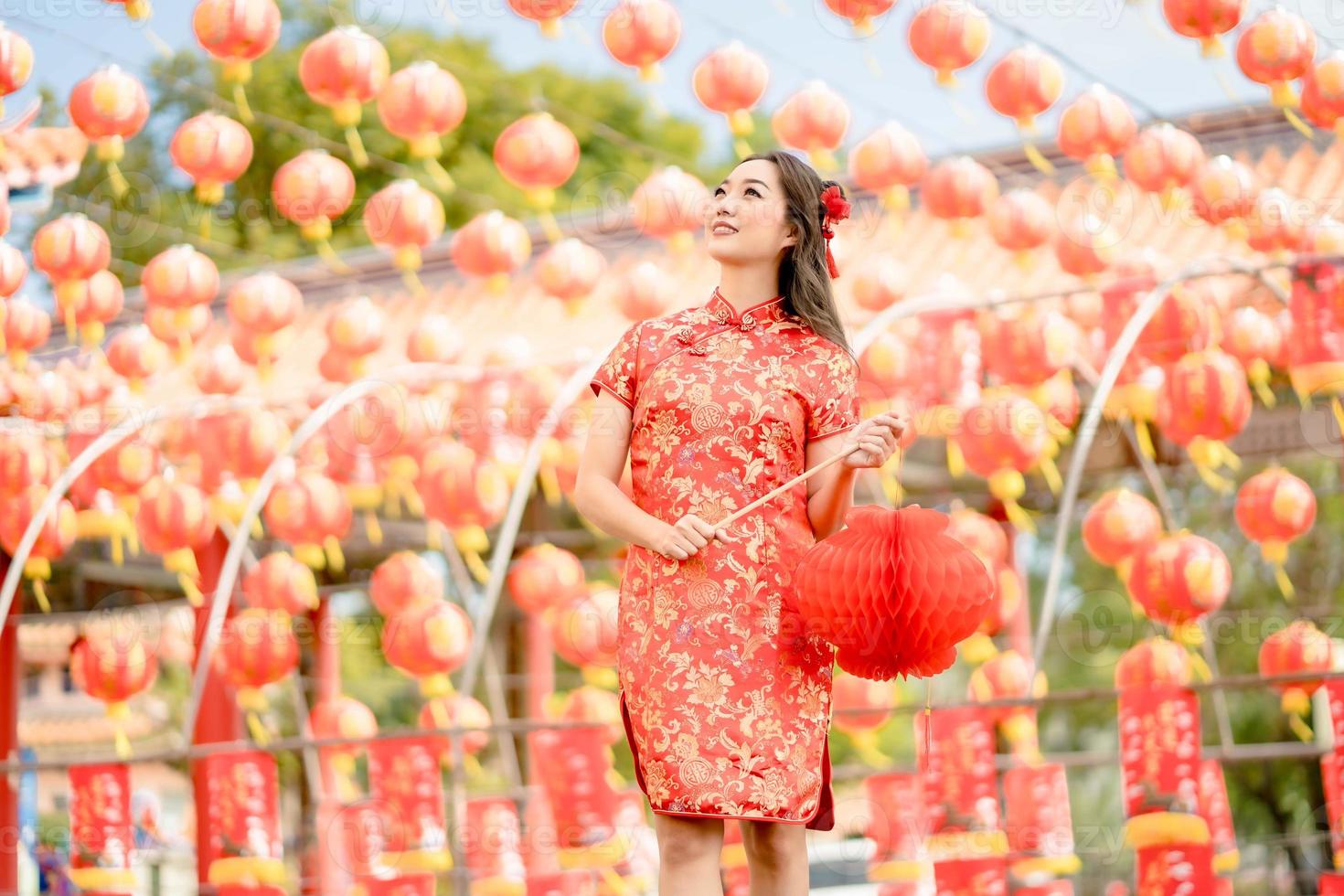 jovem mulher vestindo traje tradicional cheongsam qipao segurando lanterna no templo budista chinês. comemore o ano novo lunar chinês, feriado da temporada festiva. sorriso de emoção foto