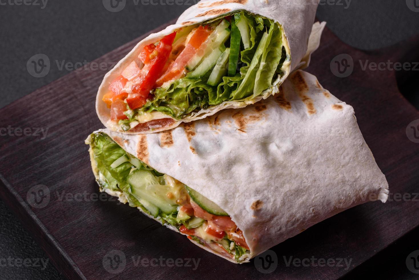 delicioso shawarma fresco com tomate, pimentão, pepino em um fundo escuro de concreto foto