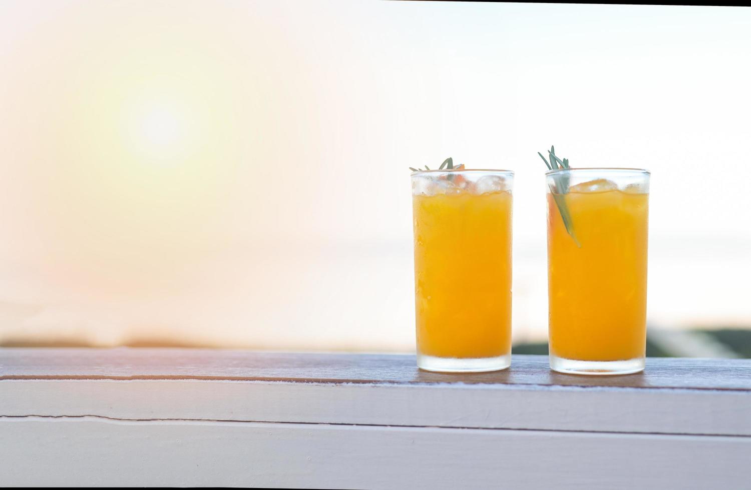 copo de suco de laranja na mesa de madeira, suco de laranja fresco com fruta laranja e alecrim no fundo da natureza vista de manhã foto