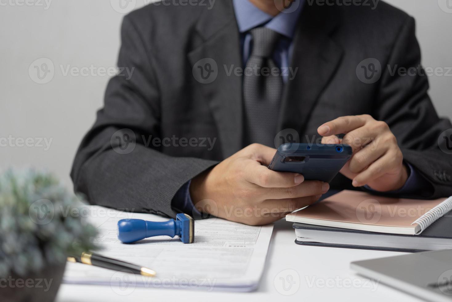 empresário usando smartphone e trabalhando em documentos no escritório, homem segurando o telefone lendo recibos bancários, impostos, dinheiro, finanças, despesas de empréstimo ou papelada de trabalho. foto