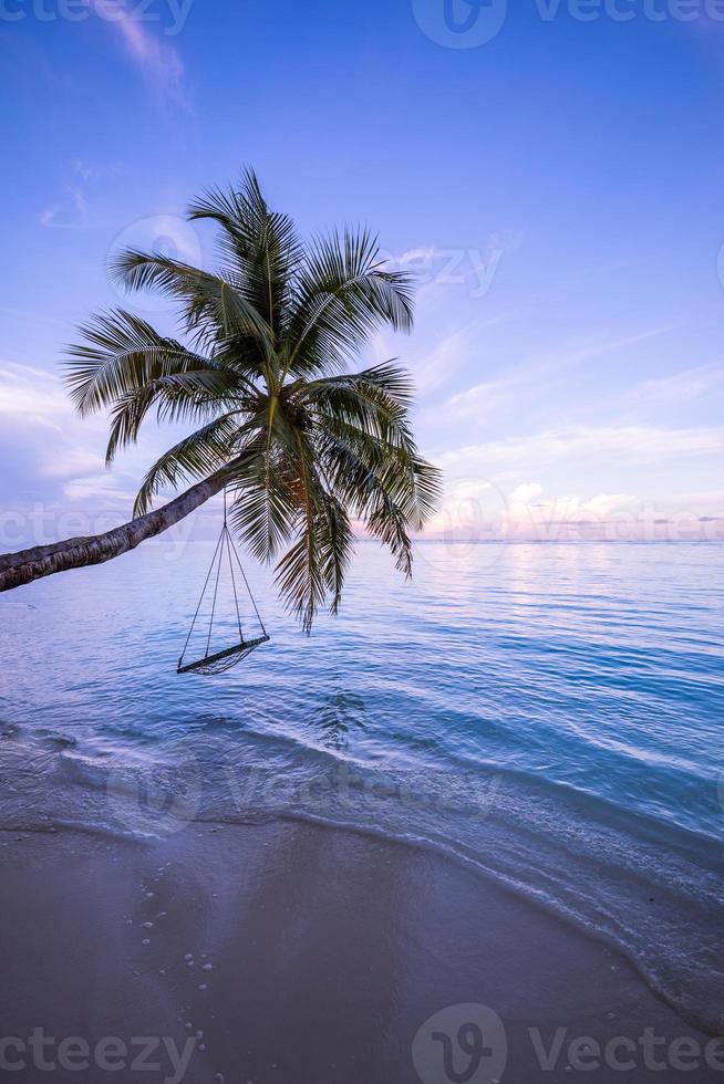 uma vista de uma praia com palmeiras e balanço ao pôr do sol. paisagem única, paraíso sereno e pacífico. cenário romântico perfeito do pôr do sol na praia, mar calmo, céu colorido. belo padrão de natureza tropical foto