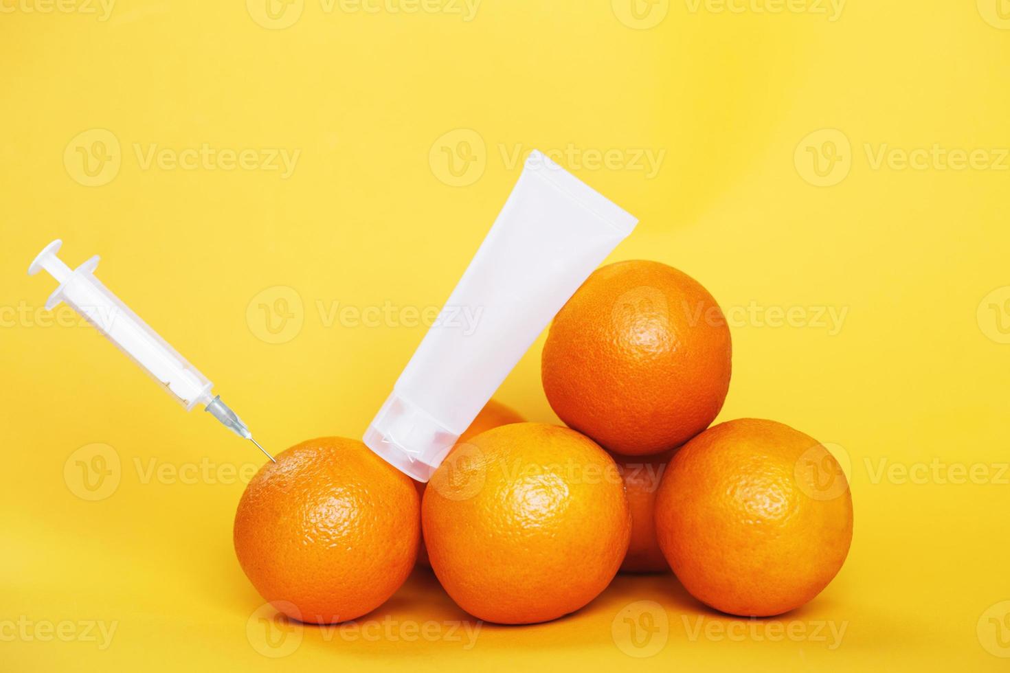frutas laranja com seringa extraindo líquido com vitamina c e tubo de creme vazio. conceito de cosméticos naturais antienvelhecimento foto