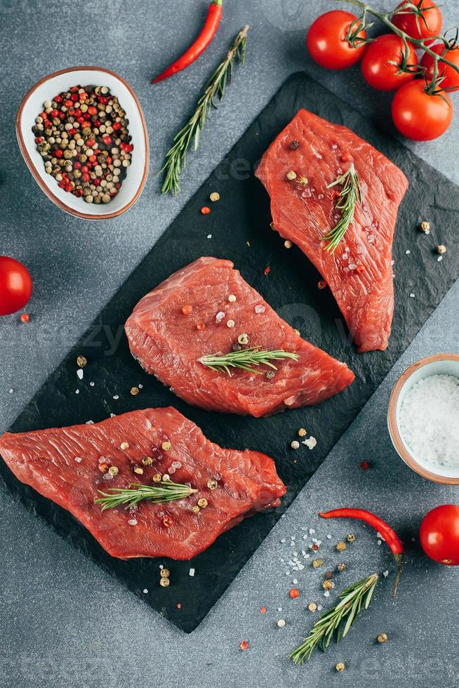 carne crua. bife de carne crua em uma placa preta com ervas e especiarias. vista do topo. foto