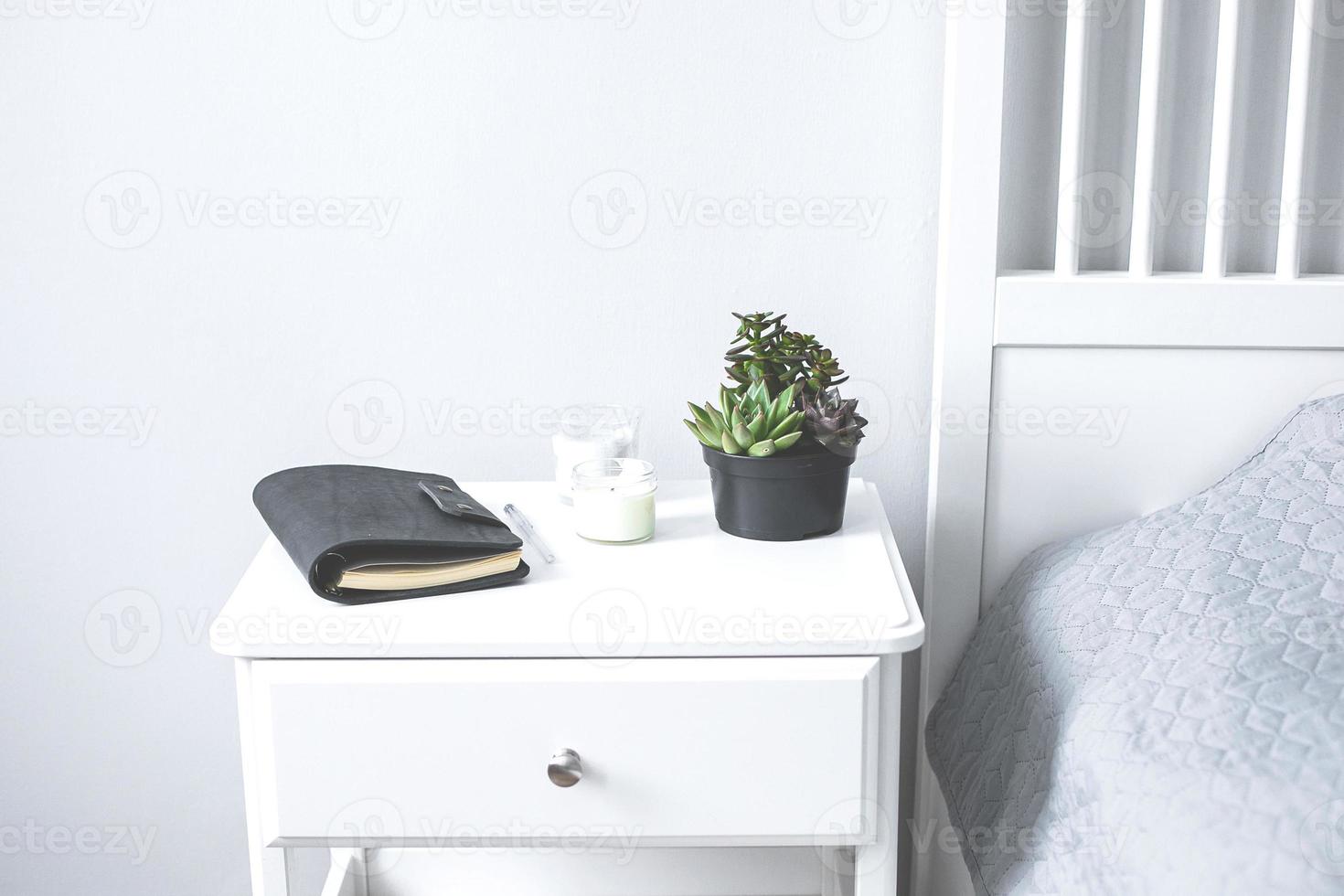 suculentas minúsculas, velas e caderno preto na mesa de cabeceira no quarto em estilo escandinavo foto