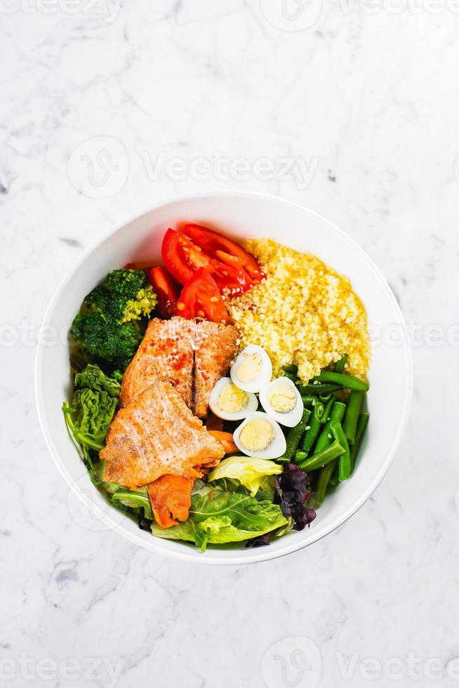 refeição saudável, conceito de comida ceto. tigela de salada de peixe no fundo da mesa de mármore. salada com salmão, cuscuz, legumes, ovos de codorna. vista superior, copie o espaço foto