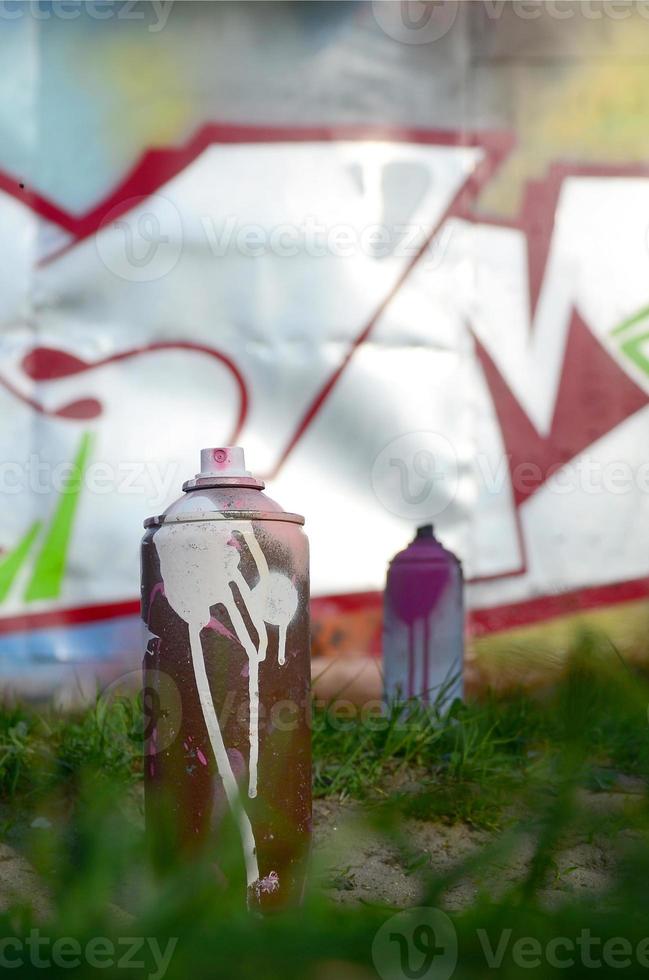 algumas latas de tinta usadas estão no chão perto da parede com uma bela pintura de grafite. arte de rua e conceito de vandalismo foto