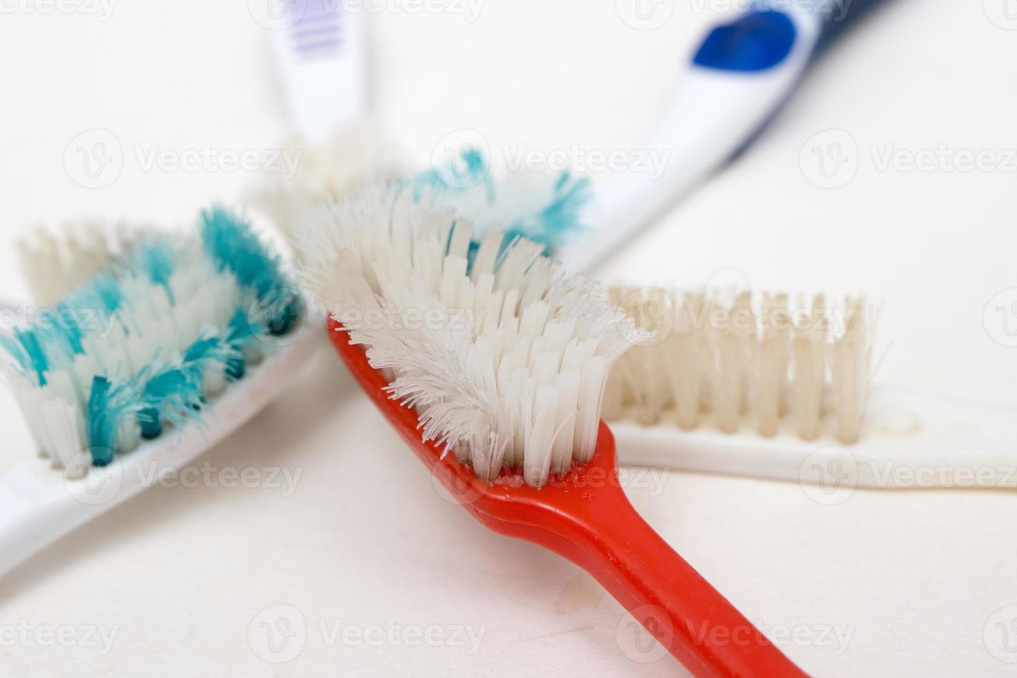 um monte de velhas escovas de dentes desgastadas com cerdas dobradas em um fundo branco foto