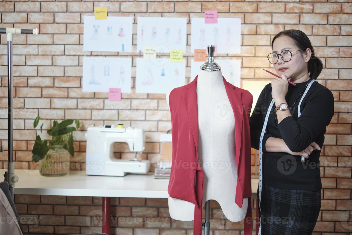 designer de moda feminina madura asiática fica perto de vestir fantoche, pensando e contemplando ideias de design em estúdio, trabalha com coleção de roupas, alfaiate profissional empresária de sme. foto