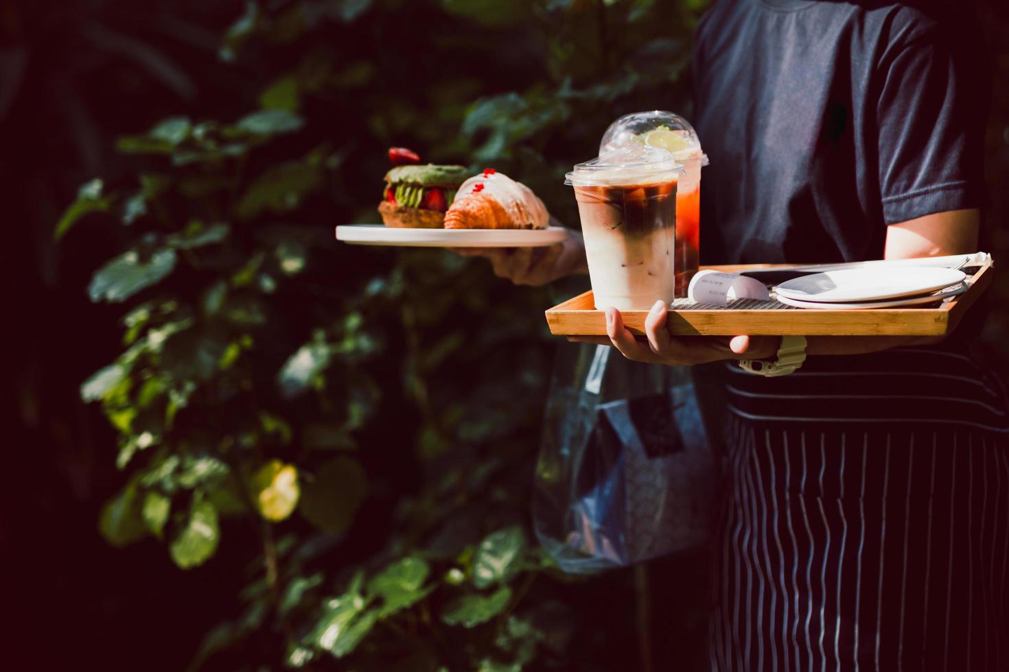 garçonete servindo café gelado e croissants no café ao ar livre. foto