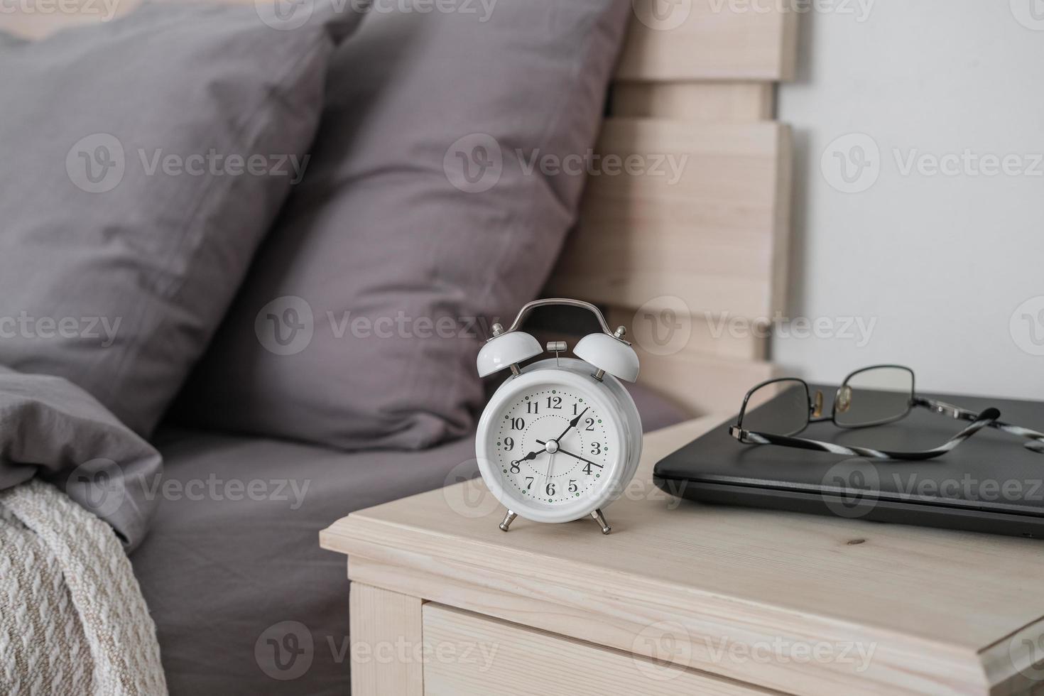 despertador, laptop e óculos na mesa de cabeceira. trabalho remoto no conforto da sua casa. escritório em casa aconchegante foto