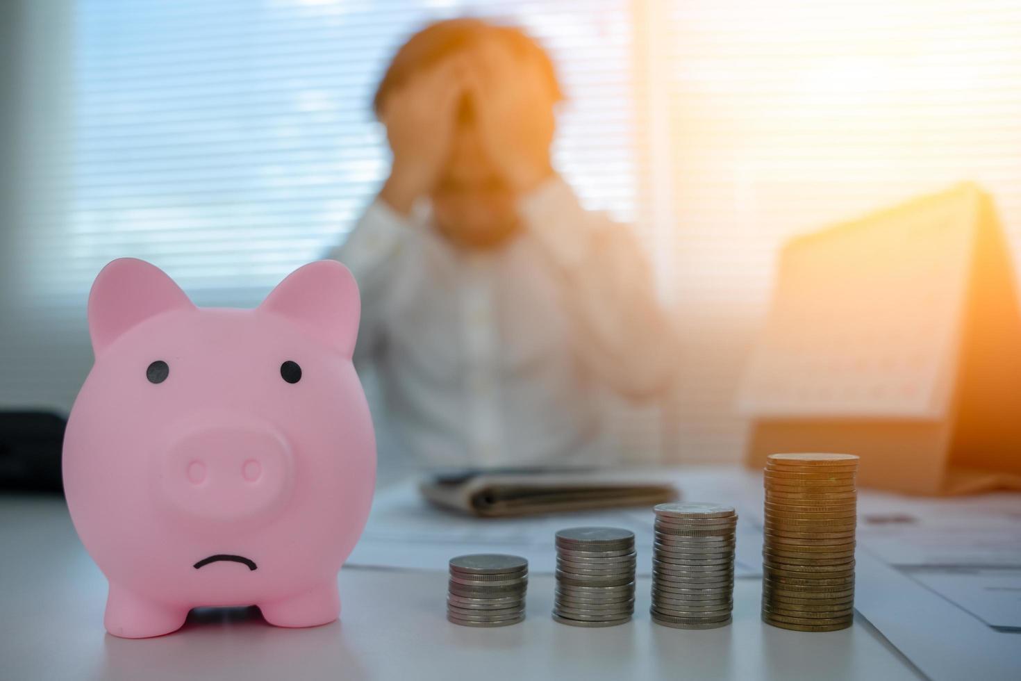 cofrinho triste com foco de moedas de pilha. borrão homem estressado com problemas de dívida e despesas, sem dinheiro para pagar, cheques, cartão de crédito, falido, hipoteca, empréstimo, falência foto