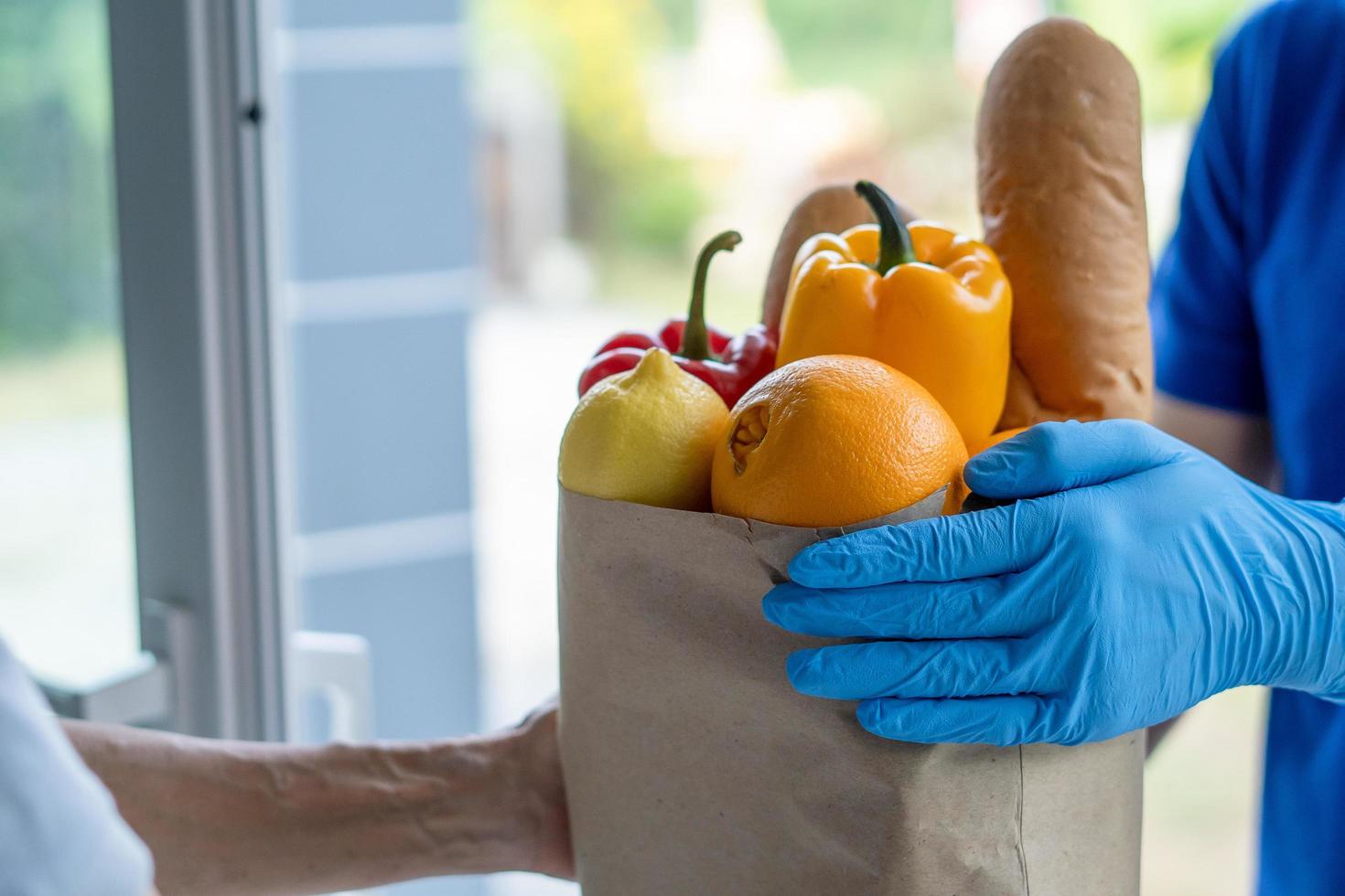 entregador envia sacolas de comida para clientes em frente a casa durante a epidemia de covid-19. remetente usa luvas de proteção. encomenda online e serviço de entrega rápida foto