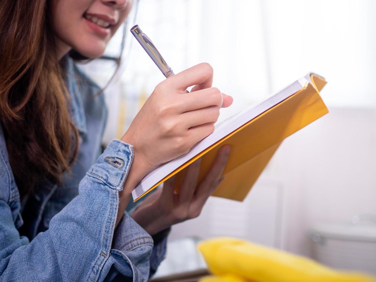 a garota escrevendo notas com uma caneta em um livreto amarelo feliz por estar no quarto em casa. foto