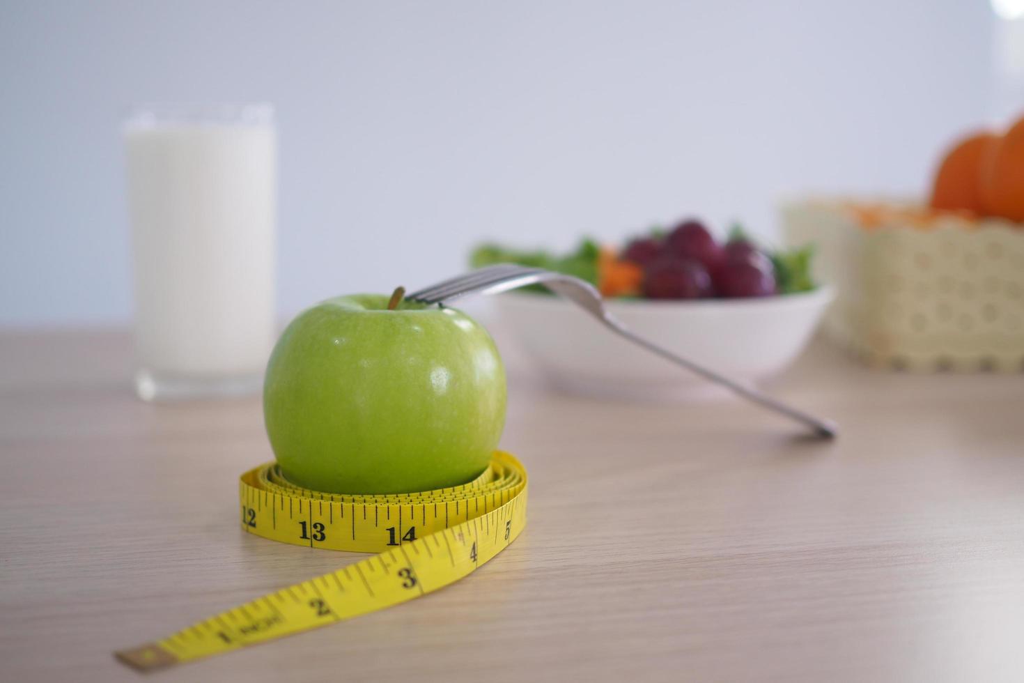 fita métrica ao redor da maçã verde. em seguida, há leite e salada de legumes na mesa de madeira. comer para uma boa saúde e perda de peso. conceito de dieta foto