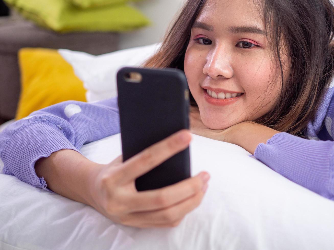 a menina sorriu e curtiu uma videoconferência com um amigo ou namorado usando uma câmera de celular enquanto estava deitada na cama em casa. fique em casa e feliz foto