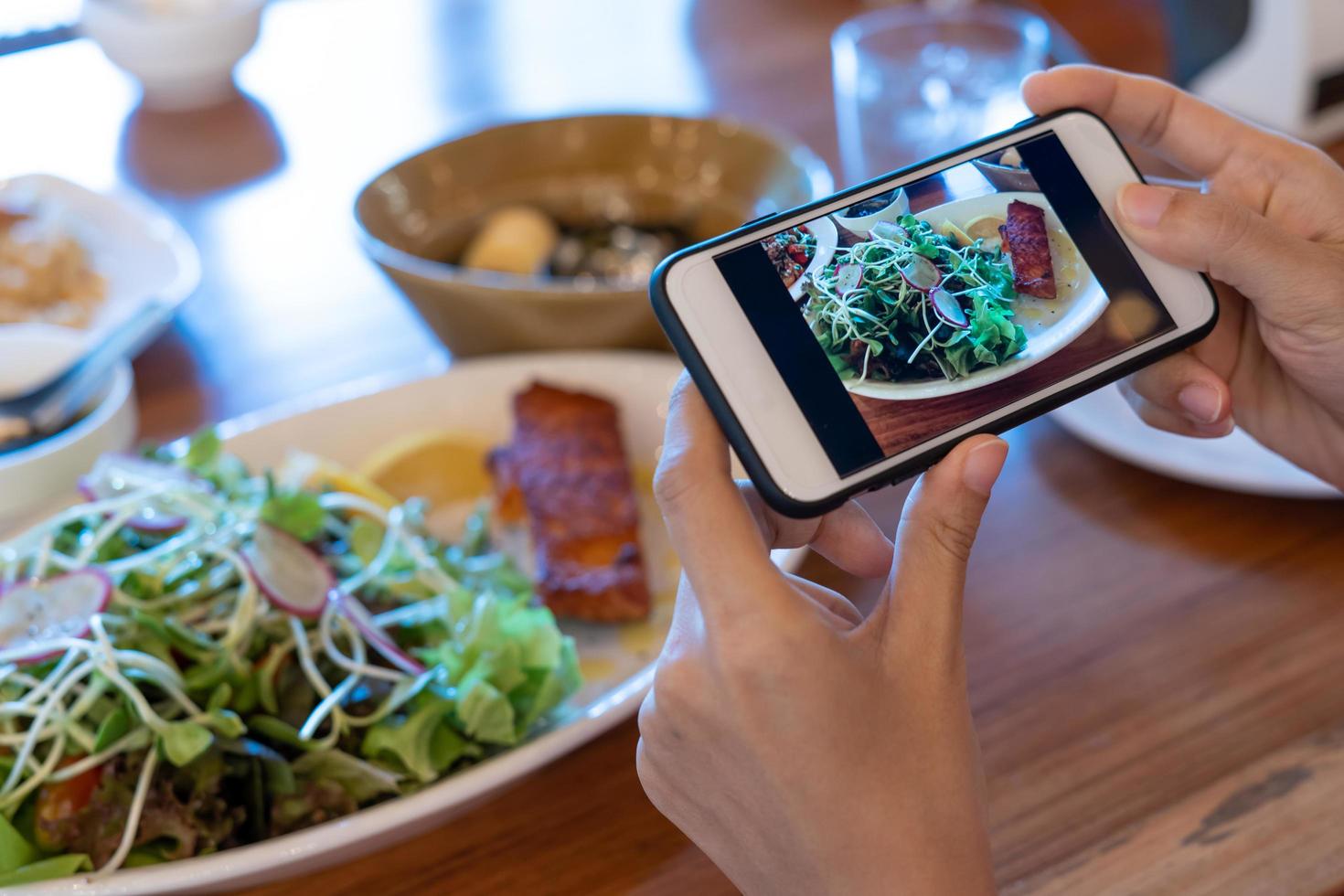 mão de mulher tira foto do café da manhã com um smartphone na mesa. mulher usa o telefone para tirar fotos de comida para revisar ou fazer upload de mídia social.