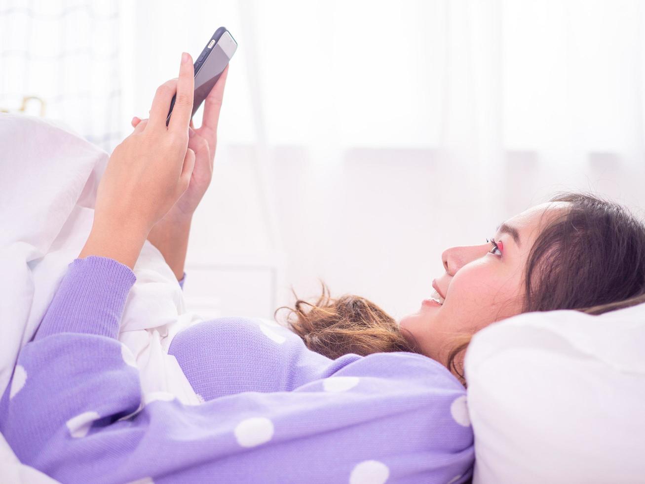 mulher deitada na cama no quarto relaxando jogando jogos online e assistindo série coreia online com um smartphone durante introvertido, fique em casa e não saia de casa. foto