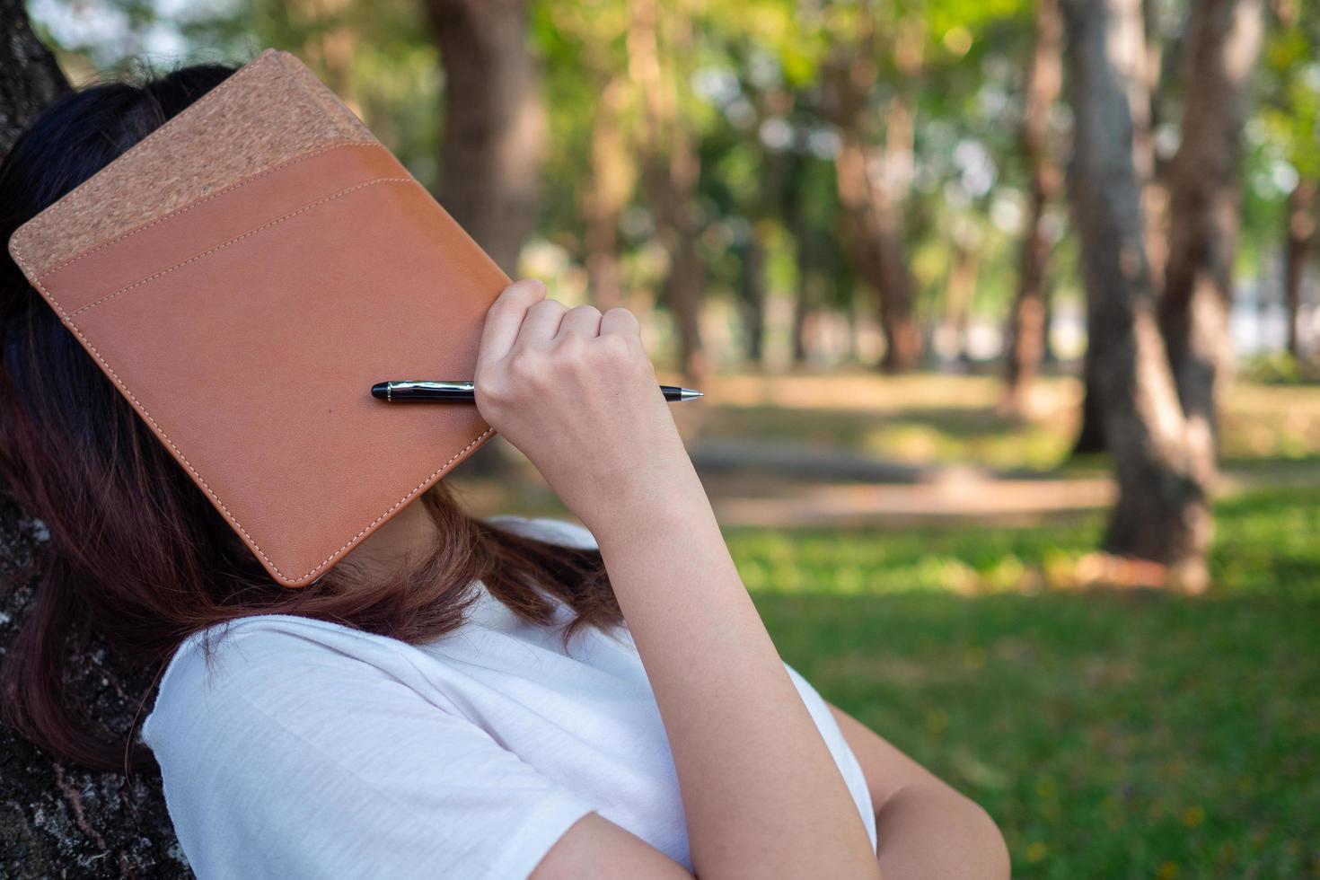 mulheres asiáticas usam camisas brancas. sentado e lendo debaixo de uma árvore no jardim e adormeceu descansando com uma folha de rosto. dia de preguiça foto