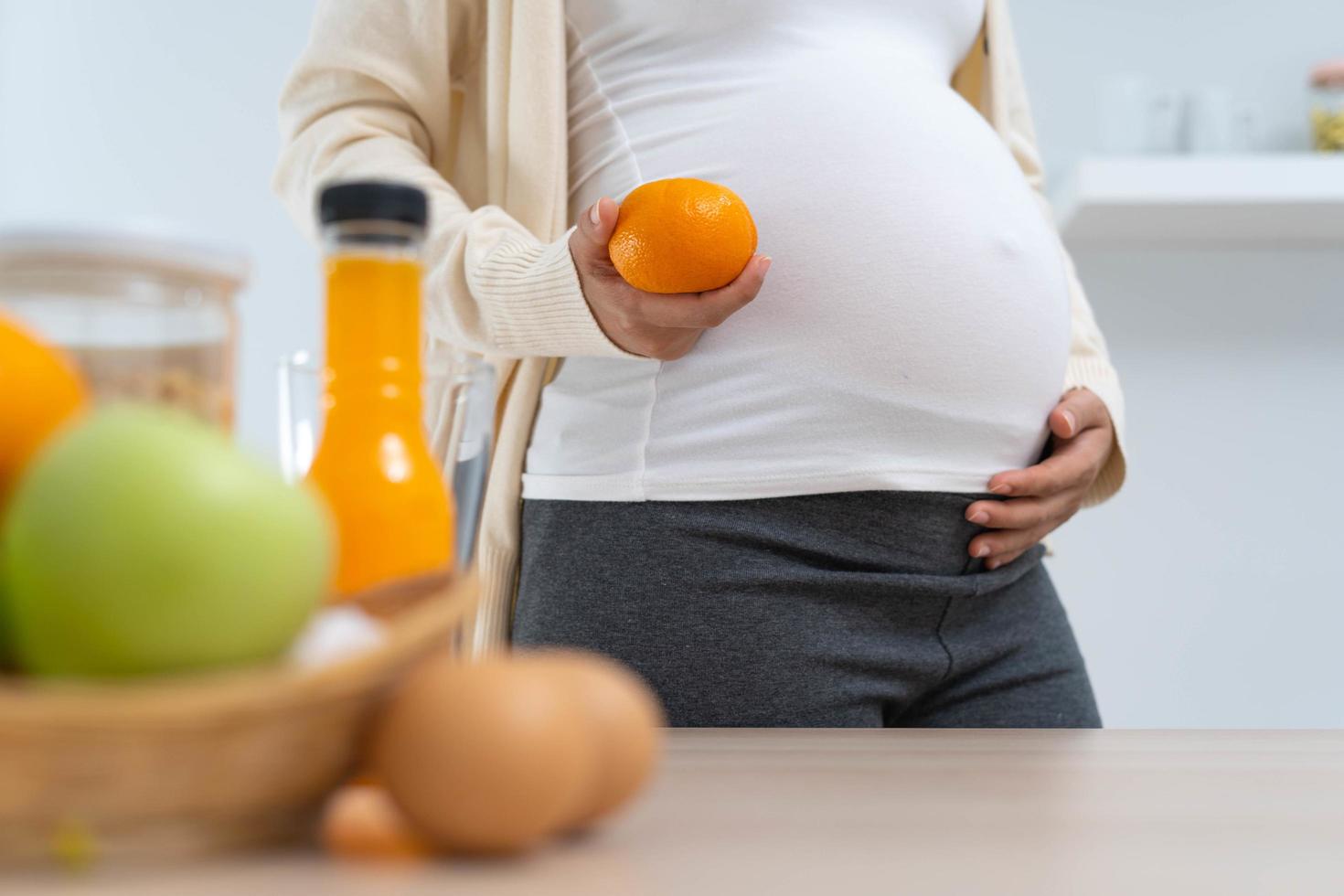 uma mulher grávida de 28 semanas segura uma laranja e escolhe uma dieta nutritiva para o desenvolvimento saudável e o crescimento de seu filho ainda não nascido. foto