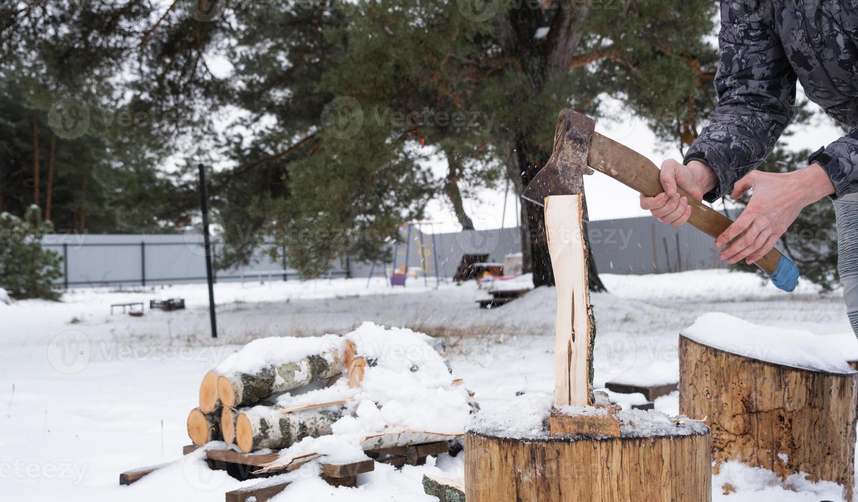 um homem está cortando lenha com um machado no inverno ao ar livre na neve. aquecimento alternativo, colheita de madeira, crise energética foto