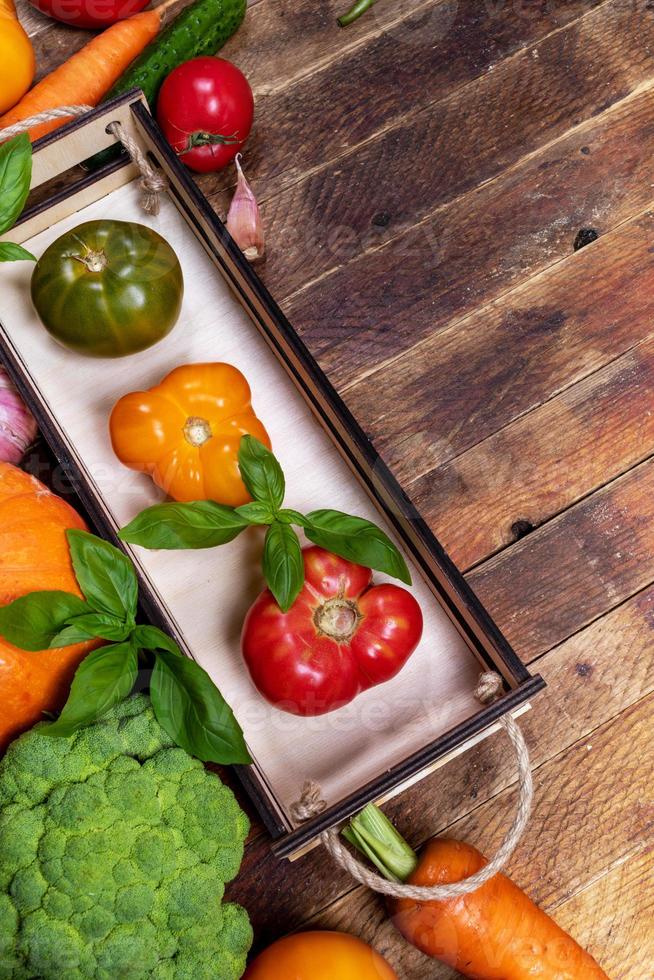 pequena caixa de madeira com tomates frescos maduros de fazenda e legumes na velha mesa rústica com espaço de cópia. foto