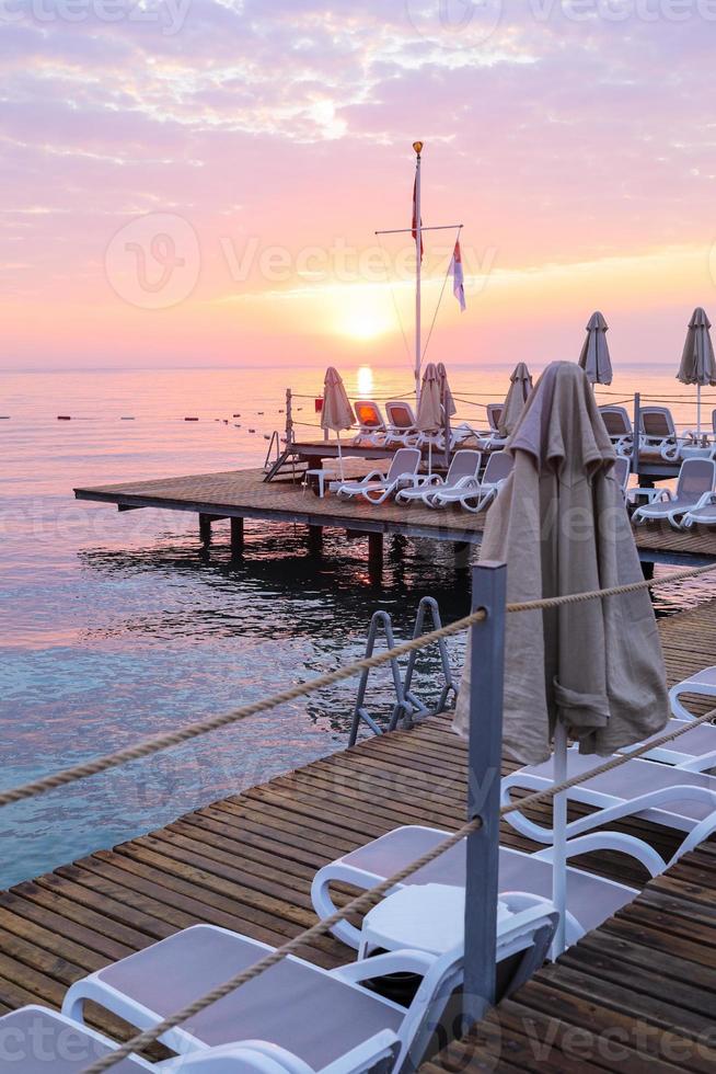 vista do romântico céu do nascer do sol, mar e plataforma com espreguiçadeiras e guarda-sóis vazios. foto