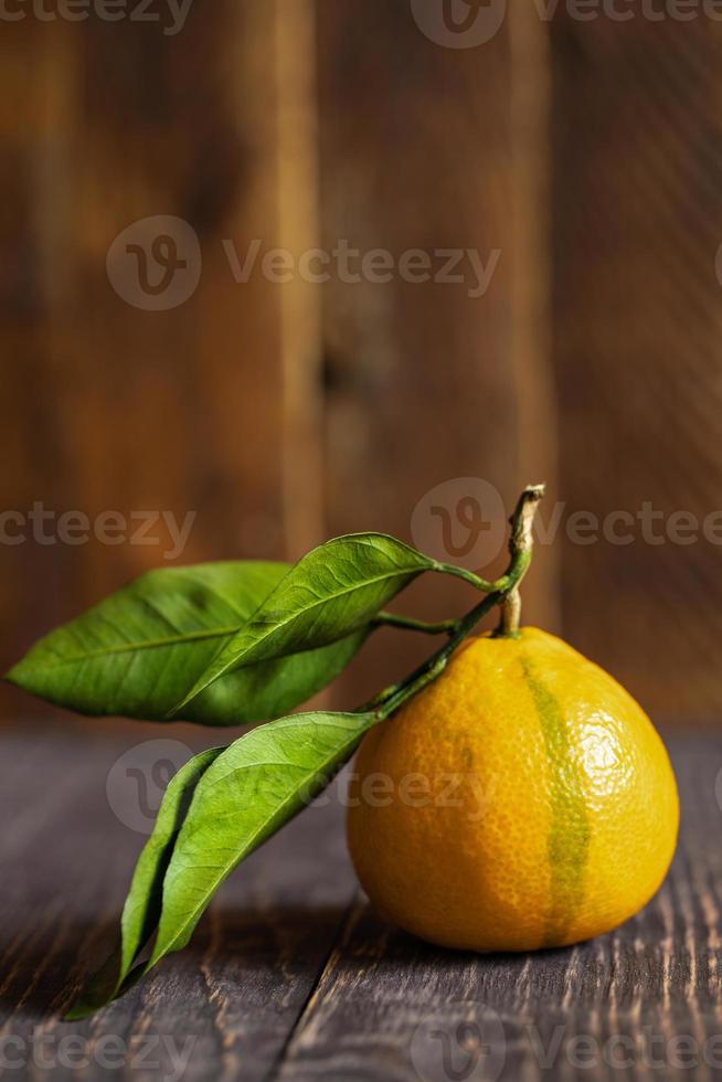 um mandarim amarelo com folhas está deitado na mesa de madeira com fundo de madeira. foto