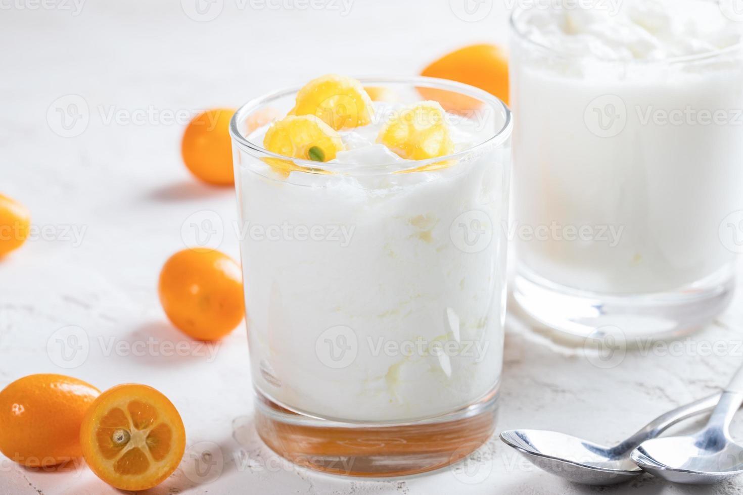 dois copos com iogurte com fatias de kumquat e duas colheres em fundo branco. foto