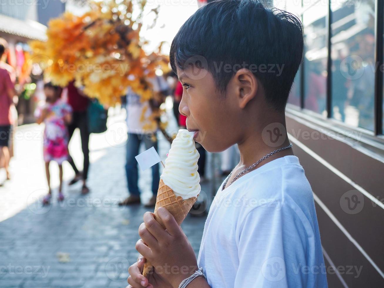 um menino vestindo uma camisa branca está comendo sorvete. foto