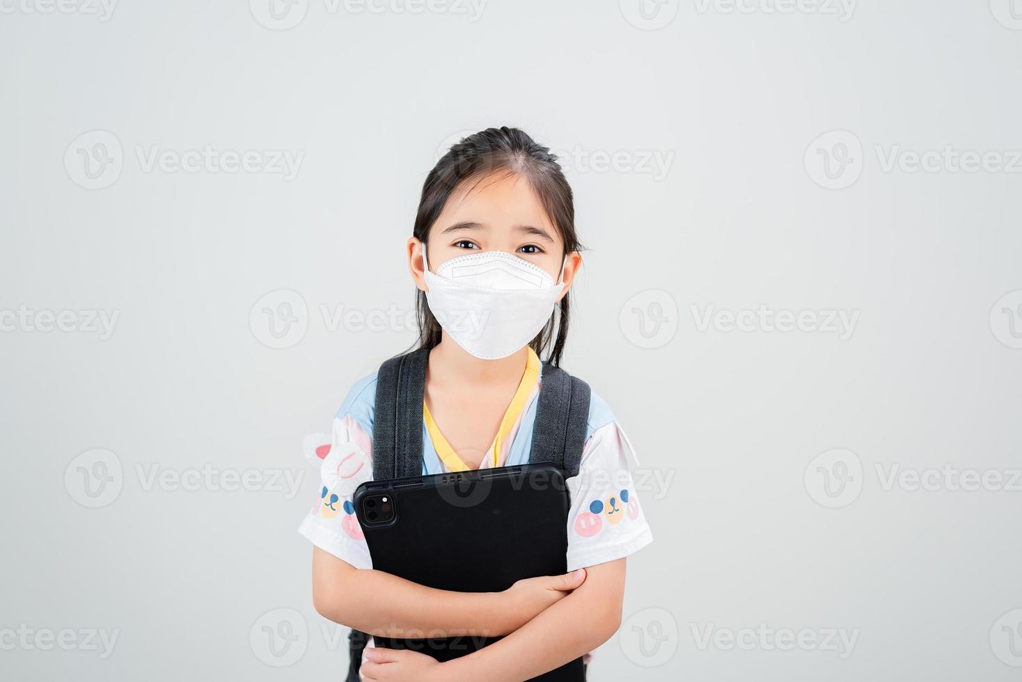 menina asiática carrega uma mochila usando máscara respiratória para proteger o surto de coronavírus e apontando a mão para um fundo em branco, novo vírus covid-19 foto