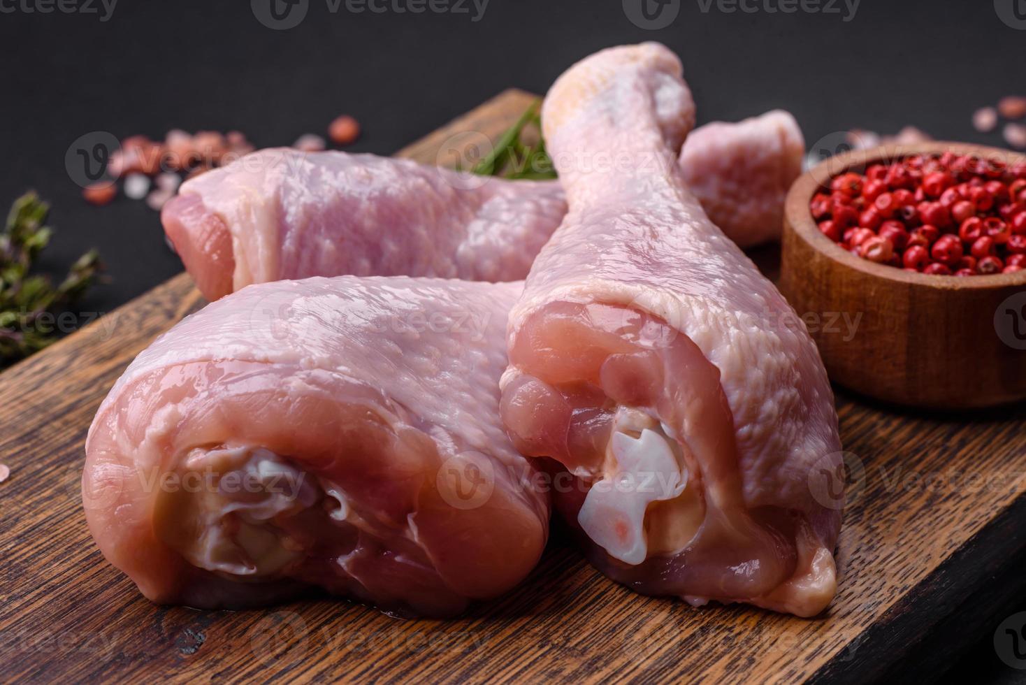 três pernas de frango cru com especiarias e ervas em uma tábua de madeira foto