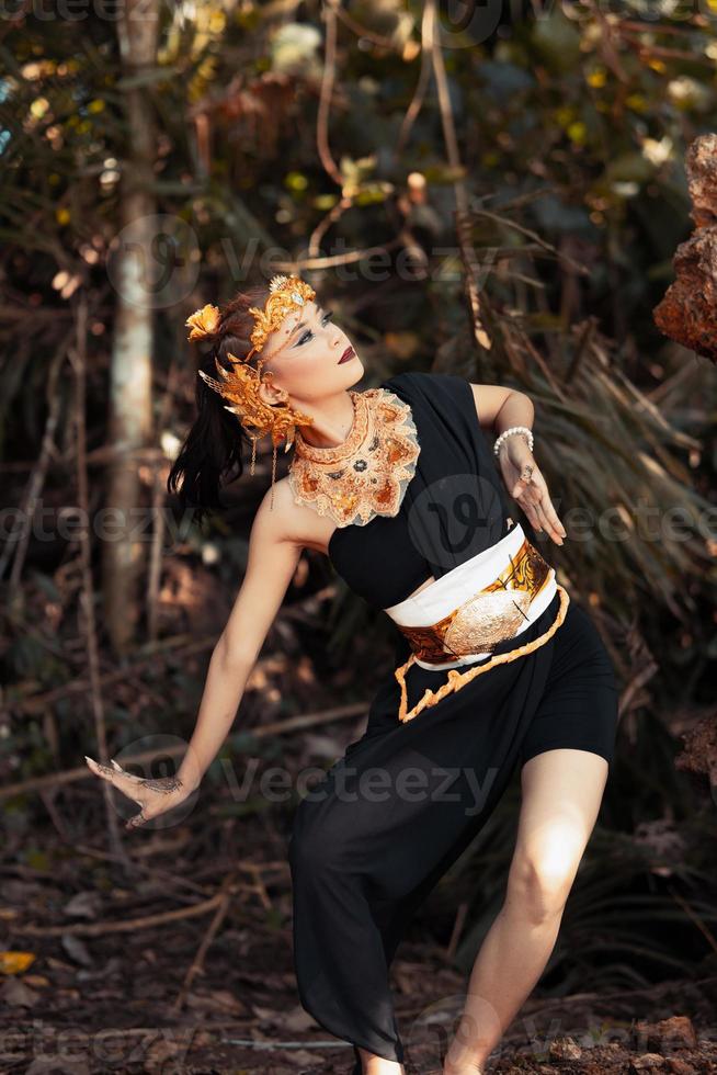 mulher antiga em sua coroa de ouro e pose de colar de ouro em seu vestido preto dentro da floresta foto