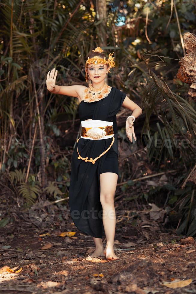 pose de dança de mulher javanesa em um top preto e saia preta com coroa dourada e acessórios dourados em seu corpo dentro da selva foto