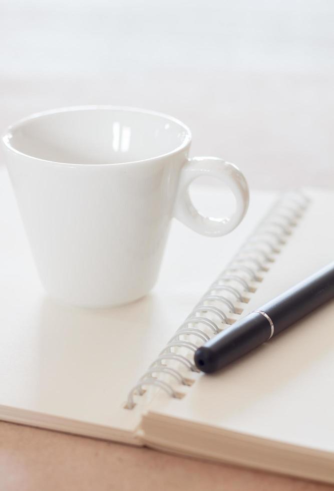 caneta e um caderno espiral com uma xícara de café foto