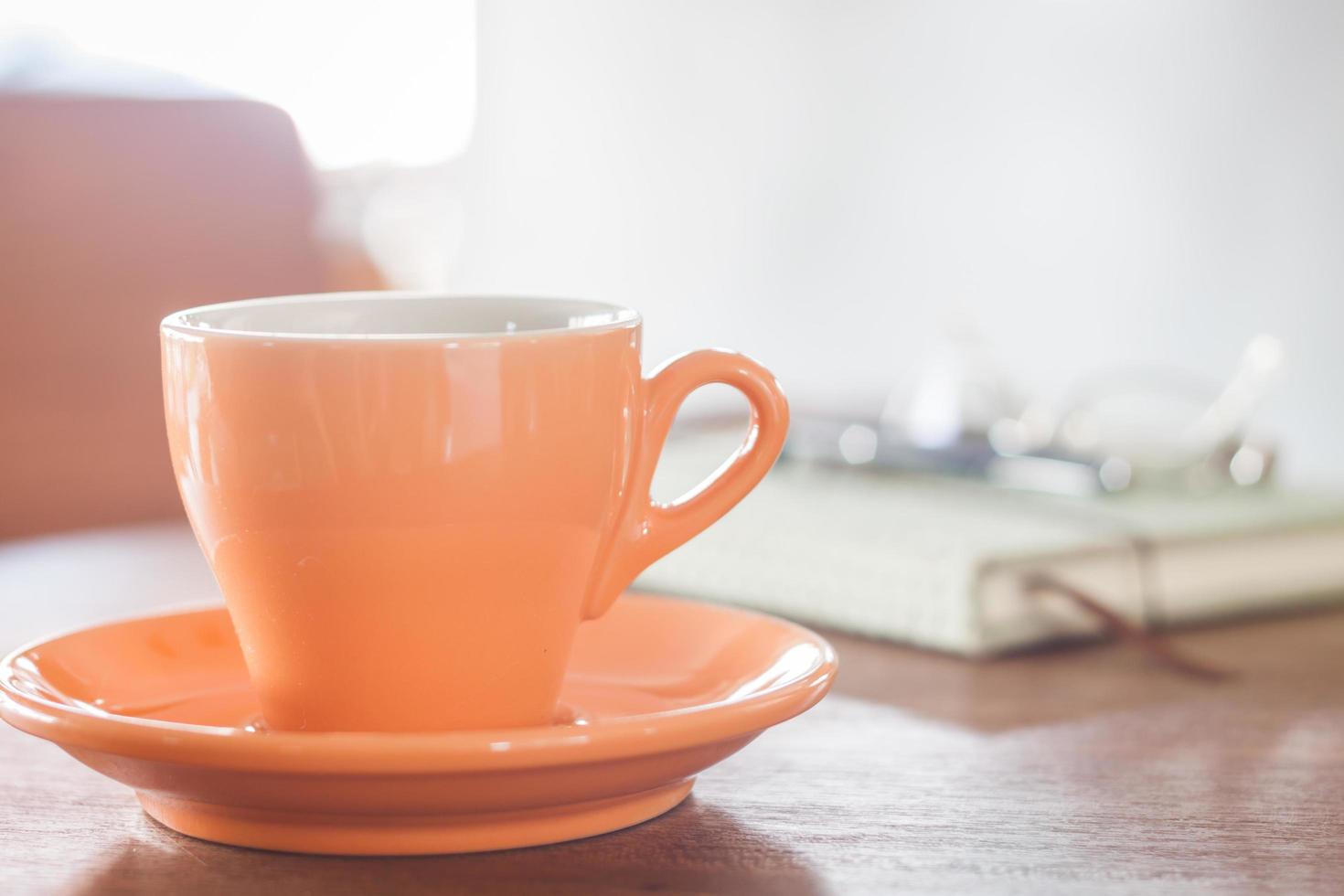 xícara de café laranja com um caderno, caneta e óculos foto