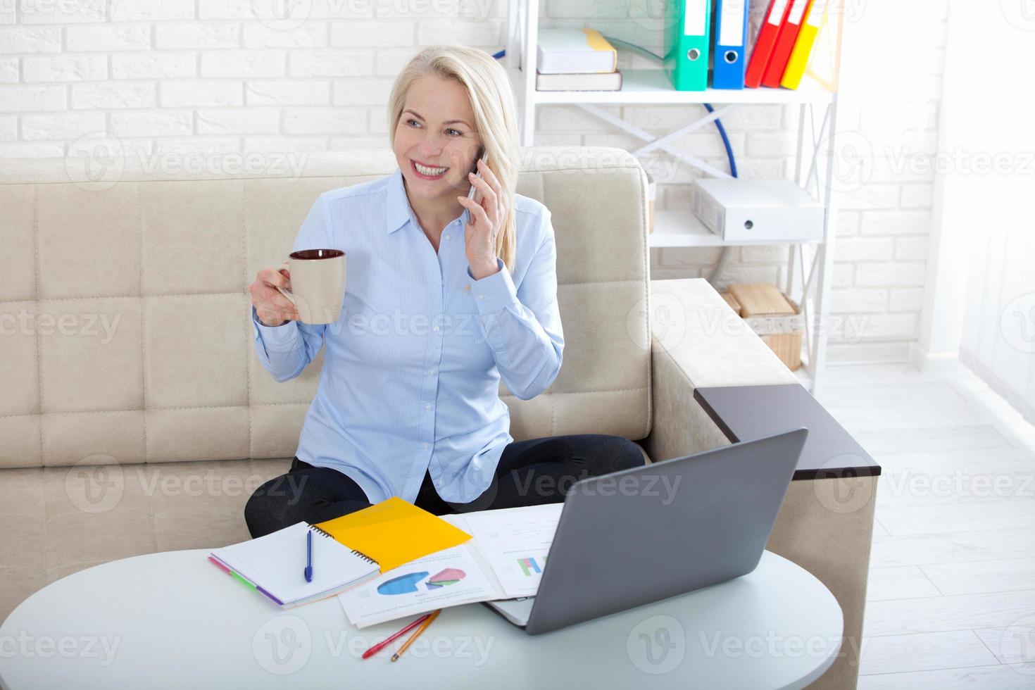 ouvir os requisitos dos clientes. linda mulher de meia idade com óculos falando no telefone inteligente e sorrindo em seu local de trabalho no escritório. foto