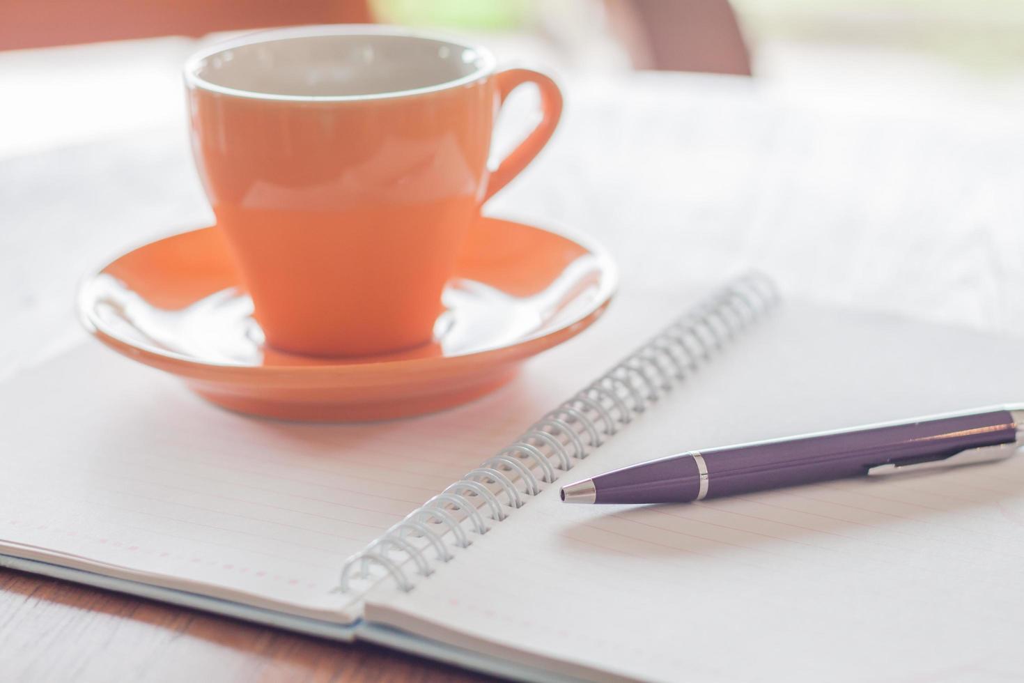 xícara de café, uma caneta e um caderno em uma mesa de madeira foto
