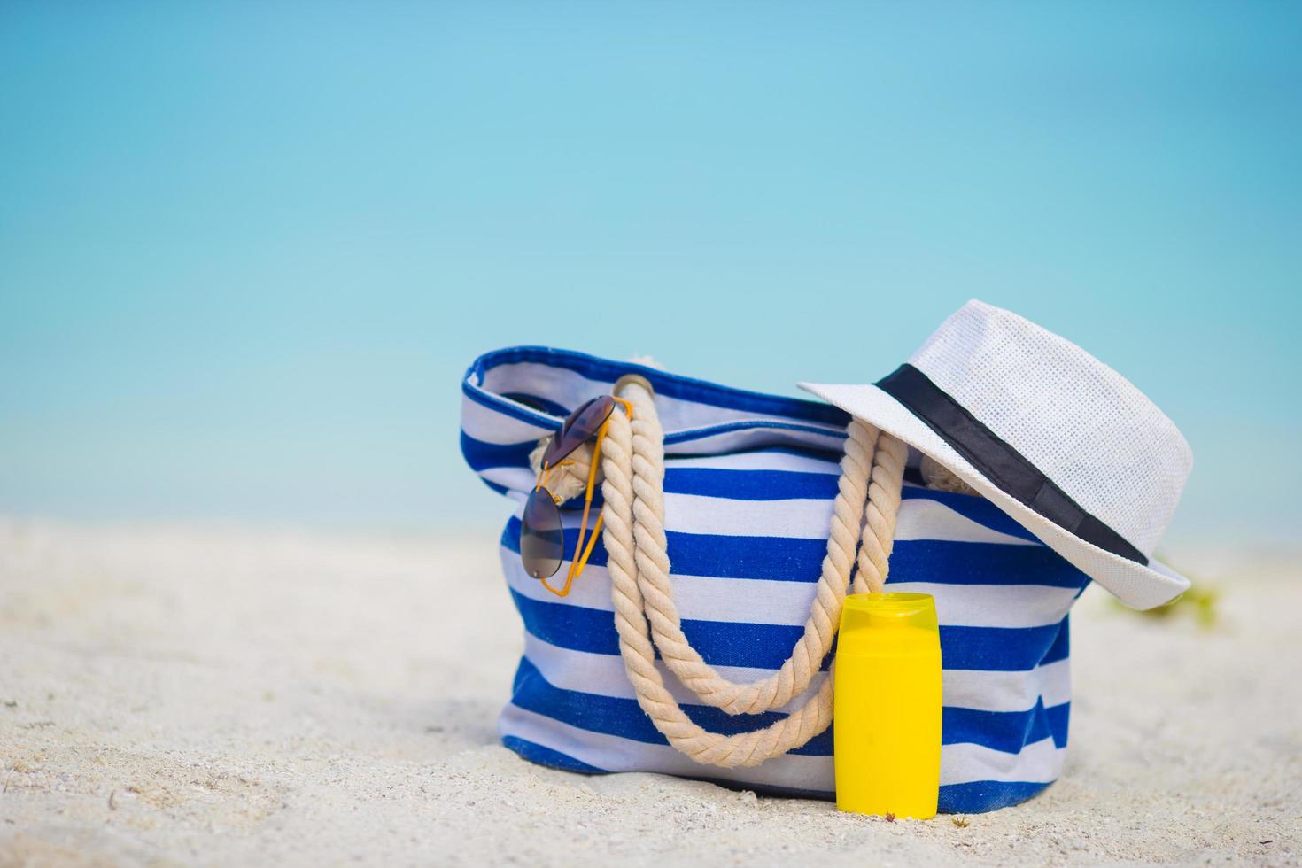 close-up de uma bolsa listrada de azul e um chapéu na praia foto